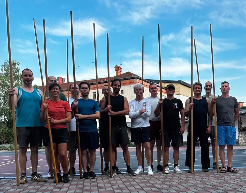 Grupo de practicantes con palos largos en una cancha al aire libre durante el campamento de Miskolc.